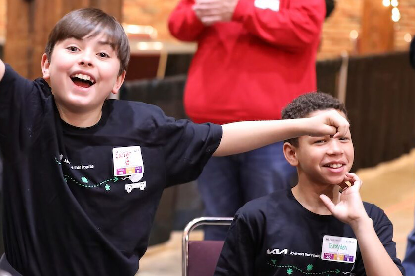 Two students in A World In Motion shirts react during an AWIM activity, with a volunteer behind them
